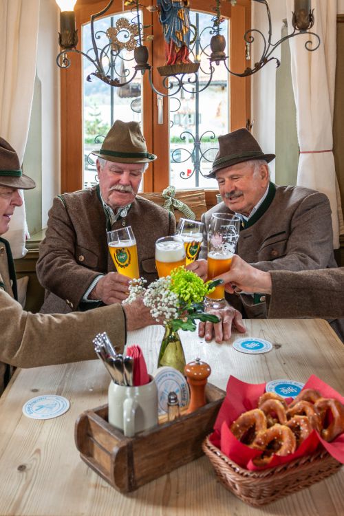 Einheimische sitzen am Stammtisch und stoßen mit Weißbier an, dazu gibt es frische Brezn